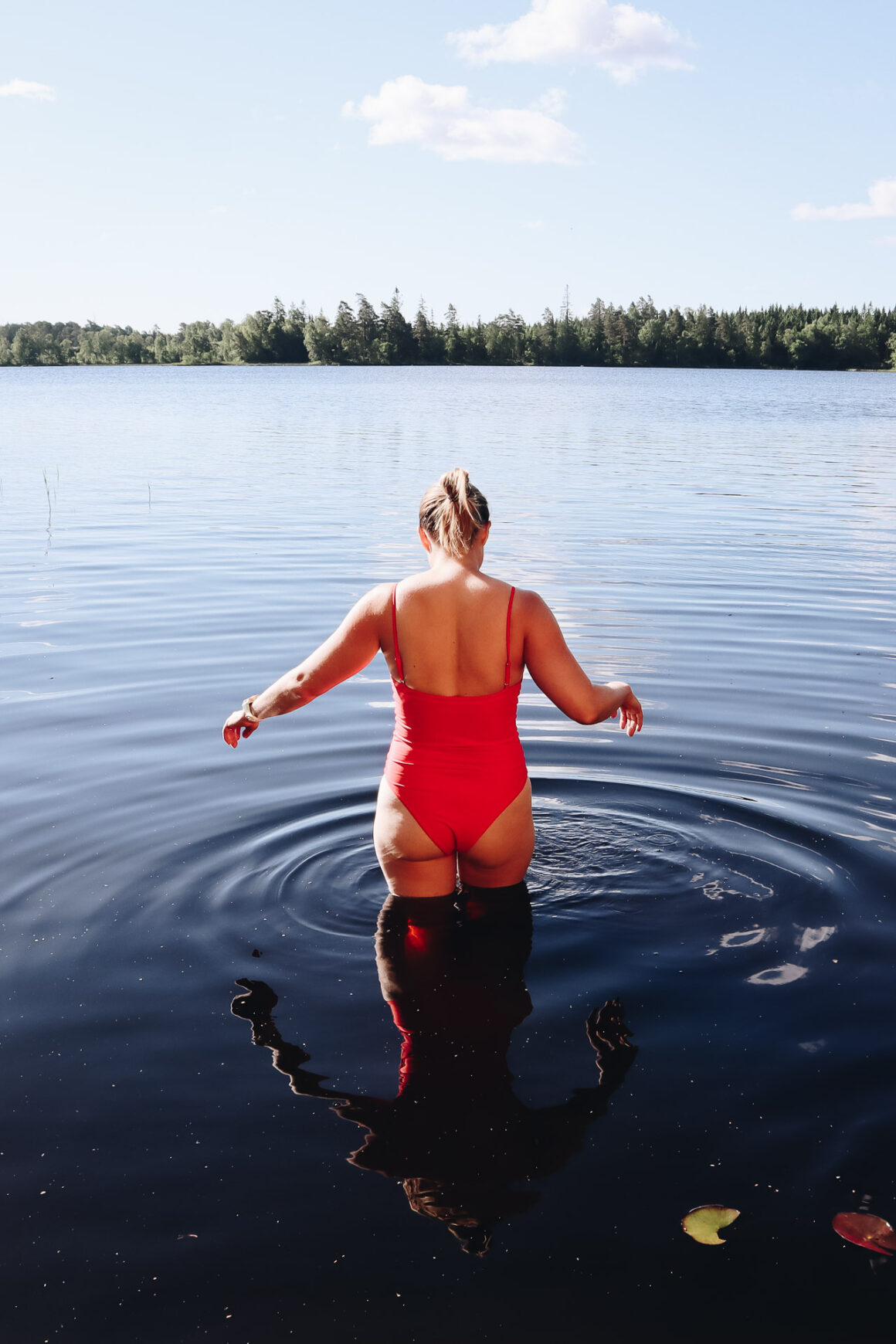 kvinna i röd baddräkt badar i svensk skogssjö